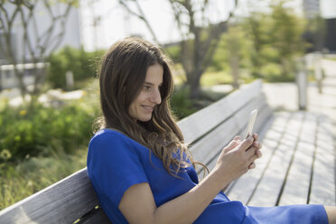 Smiling businesswoman sitting on a bench looking at smartphone - RIBF000289