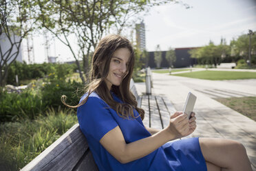 Portrait of smiling businesswoman sitting on a bench with phablet - RIBF000290