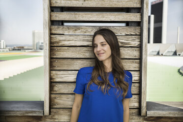 Germany, Frankfurt, portrait of smiling woman leaning against wooden wall - RIBF000291