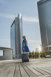 Deutschland, Frankfurt, Geschäftsfrau mit Smartphone und Rollkoffer auf Dachterrasse - RIBF000299