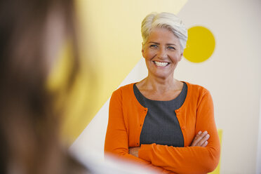 Portrait of smiling mature woman with crossed arms communicating with other person - MFF002109