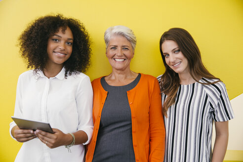 Gruppenbild von drei lächelnden Frauen, die vor einer gelben Wand stehen - MFF002112