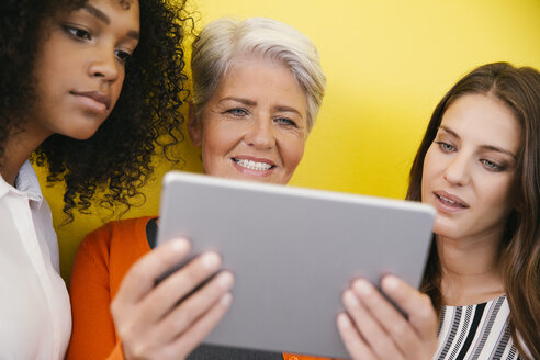 Drei Frauen schauen auf eine digitale Tafel vor einer gelben Wand - MFF002115