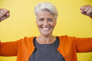 Portrait of mature woman standing like superwoman in front of a yellow wall - MFF002118