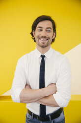 Porträt eines lächelnden reifen Mannes mit Hemd und Krawatte, der vor einer gelben Wand steht - MFF002138