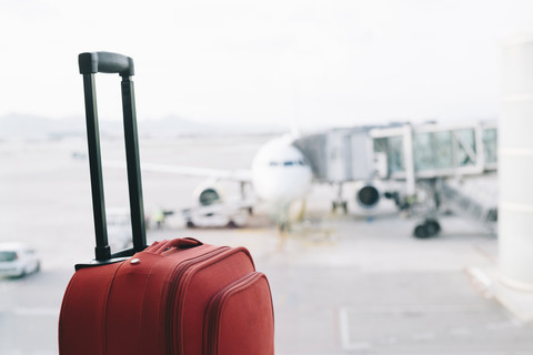 Roter Koffer am Flughafen, Flugzeug im Hintergrund, lizenzfreies Stockfoto