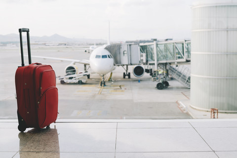 Roter Koffer am Flughafen, Flugzeug im Hintergrund, lizenzfreies Stockfoto