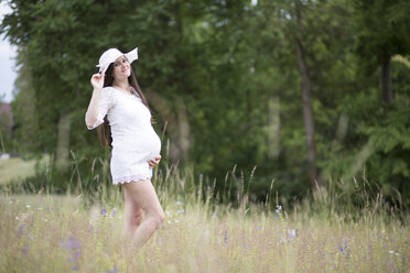 Portrait of pregnant woman wearing white clothes standing on a meadow - ASCF000375