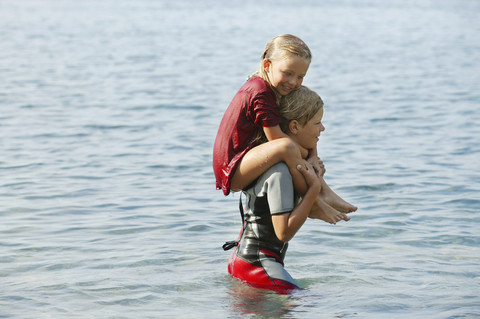 Spanien, Mallorca, Junge, der seine kleine Schwester auf den Schultern im Meer trägt, lizenzfreies Stockfoto