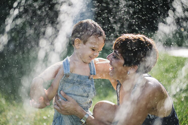 Fröhlicher kleiner Junge und seine Mutter genießen es, im Garten Wasser zu spritzen - JRFF000054