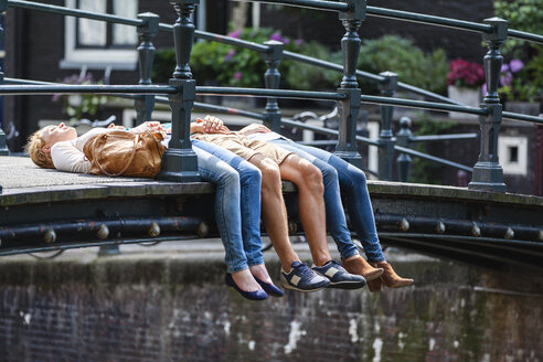 Netherlands, Amsterdam, three friends lying on bridge - FMKF002100