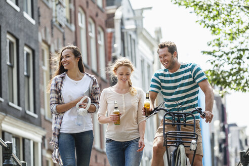 Netherlands, Amsterdam, happy friends with beer bottles and bicycle in the city - FMKF002111