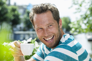 Niederlande, Amsterdam, glücklicher Mann trinkt eine Tasse Kaffee in einem Straßencafé - FMKF002119