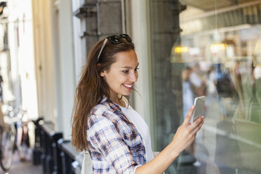 Netherlands, Amsterdam, smiling young woman in the city looking at cell phone - FMKF002135