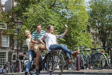 Netherlands, Amsterdam, three playful friends riding on one bicycle in the city - FMKF002146