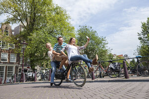 Niederlande, Amsterdam, drei verspielte Freunde fahren auf einem Fahrrad durch die Stadt - FMKF002147