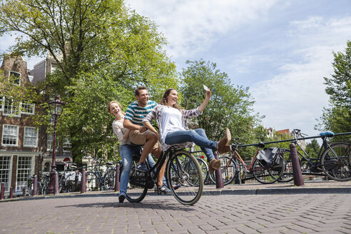 Netherlands, Amsterdam, three playful friends riding on one bicycle in the city - FMKF002147
