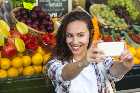 Lächelnde junge Frau macht ein Selfie im Gemüseladen, lizenzfreies Stockfoto