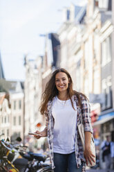 Netherlands, Amsterdam, smiling young woman in the city with cell phone - FMKF002154