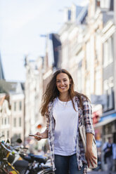 Niederlande, Amsterdam, lächelnde junge Frau in der Stadt mit Mobiltelefon - FMKF002154