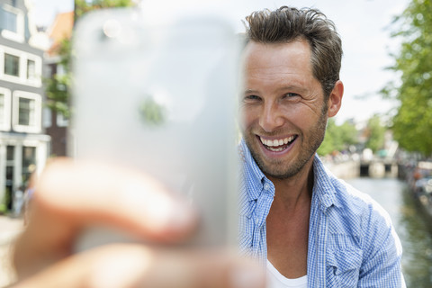 Netherlands, Amsterdam, happy man taking a selfie at town canal stock photo