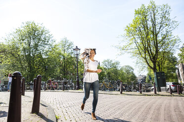 Niederlande, Amsterdam, glückliche junge Frau, die von einer Brücke läuft - FMKF002166