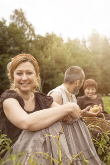 Smiling woman and two other people sitting on potato field - MIDF000628