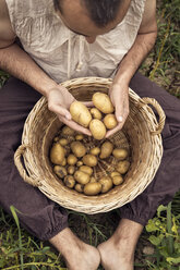 Drei Personen sitzen auf einem Feld mit Kartoffeln in einem Weidenkorb - MIDF000629