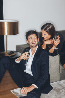 Glückliches junges Paar mit einem Glas Champagner auf dem Sofa - CHAF001438