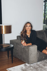 Junge Frau sitzt auf einer Couch mit einem Glas Champagner - CHAF001441