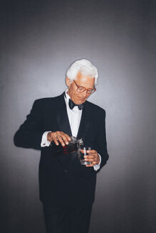 Eleganter älterer Mann gießt ein Getränk in einen Becher - CHAF001446