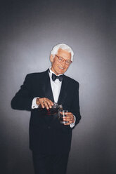 Lächelnder eleganter älterer Mann gießt ein Getränk in einen Becher - CHAF001447