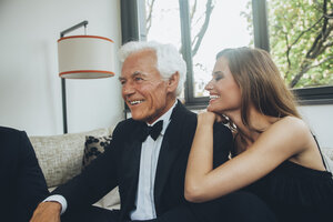 Lächelnde junge Frau mit elegantem älteren Mann auf Couch - CHAF001464