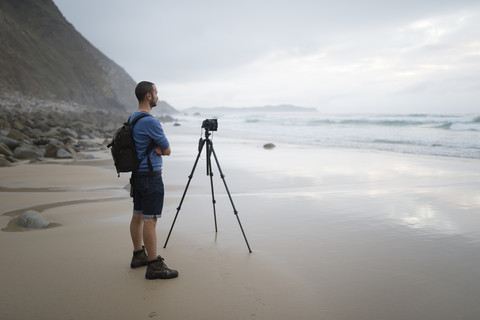 Spanien, Valdovino, Fotograf steht am Strand und fotografiert mit einem Stativ, lizenzfreies Stockfoto