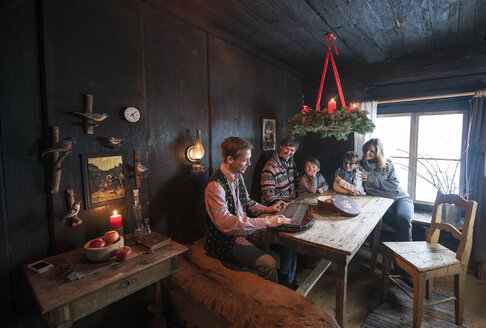 Eine Familie lauscht dem Zitherspiel eines Mannes in einer Bauernstube im Advent - HHF005406