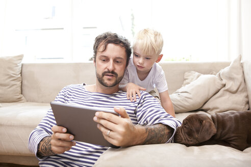 Mann und sein kleiner Sohn entspannen sich mit digitalem Tablet im Wohnzimmer - MFRF000390