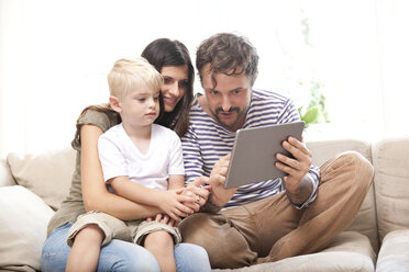 Eltern und kleiner Sohn sitzen auf der Couch mit digitalem Tablet - MFRF000455