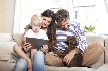 Eltern, kleiner Sohn und ihr Hund sitzen zusammen auf der Couch - MFRF000392