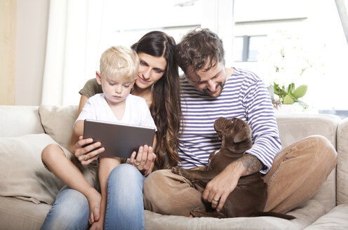Eltern, kleiner Sohn und ihr Hund sitzen zusammen auf der Couch - MFRF000392