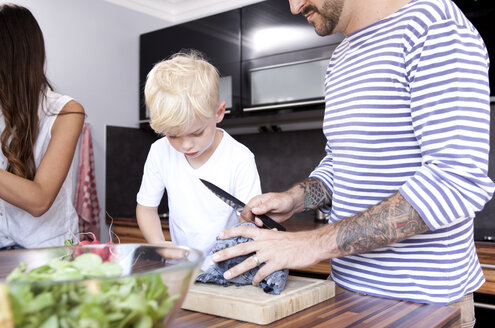Mann schneidet Rotkohl in der Küche, während sein Sohn zusieht - MFRF000399