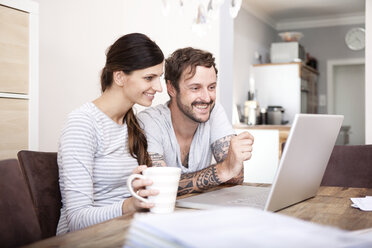 Lächelndes Paar sitzt an einem Holztisch und schaut auf einen Laptop - MFRF000421