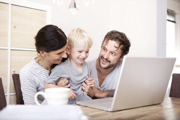 Eltern und ihr kleiner Sohn sitzen am Holztisch mit Laptop - MFRF000424