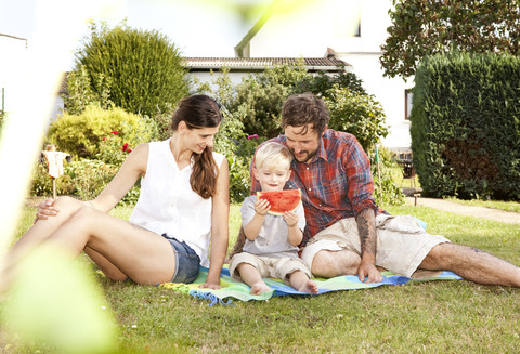 Eltern sitzen mit ihrem kleinen Sohn auf einer Decke im Garten, lizenzfreies Stockfoto