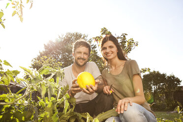 Lächelndes Paar mit gelber Zucchini im Garten - MFRF000439