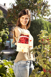 Lächelnde Frau bietet rote Johannisbeeren in einem Korb an - MFRF000441