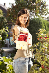 Smiling woman offering red currants in a basket - MFRF000441