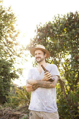 Portrait of man with tattoos on his arms standing in the garden holding bottle of beer stock photo