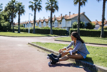 Spain, Gijon, teenage girl sitting on curb tying her roller skates - MGOF000983