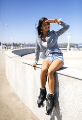 Spain, Gijon, smiling teenage girl with roller skates sitting on a wall - MGOF000994