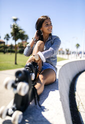 Spain, Gijon, smiling teenage girl with roller skates sitting on a wall - MGOF000996